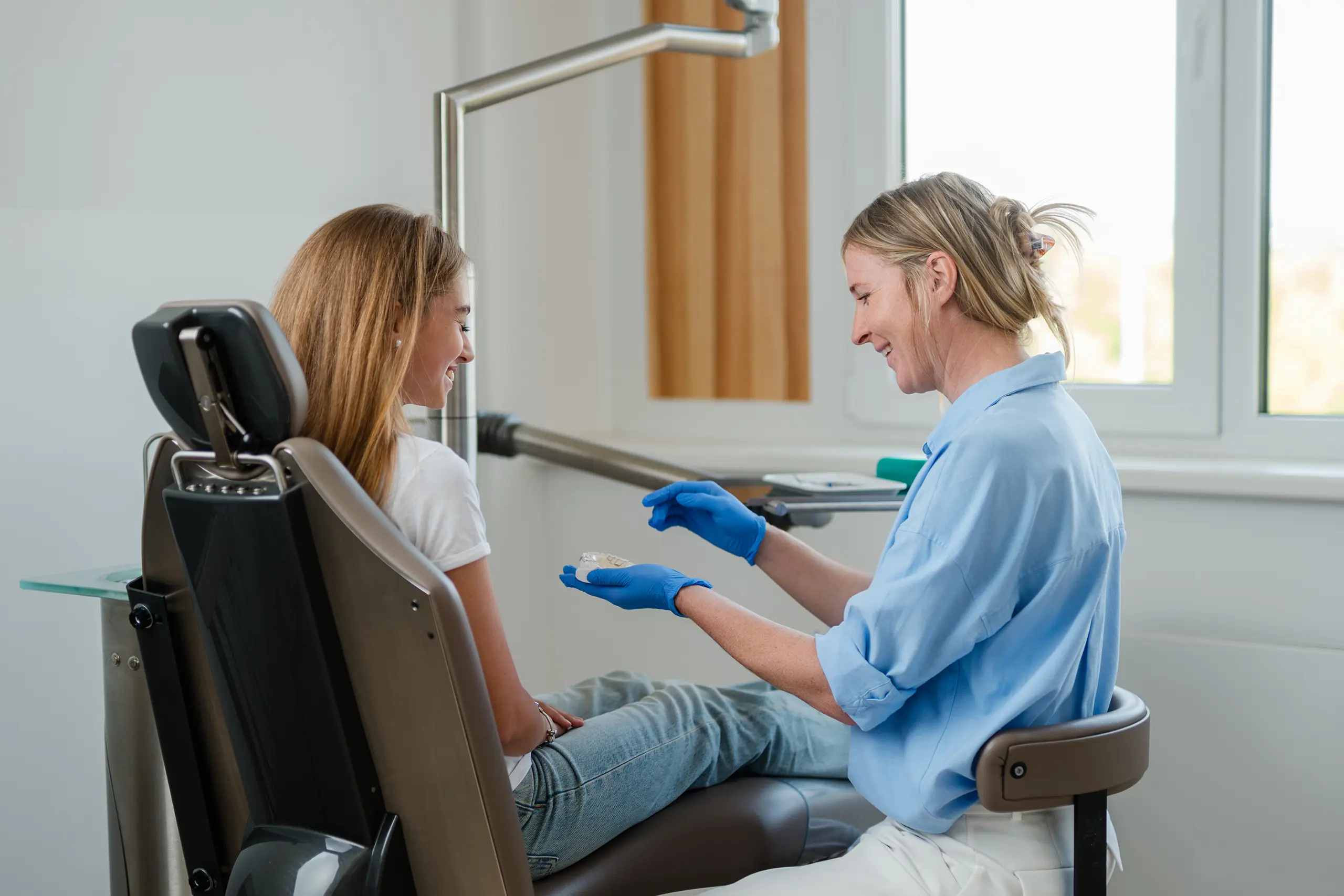 Ärztin zeigt einer Patientin auf dem Behandlungsstuhl eine transparente Zahnschiene